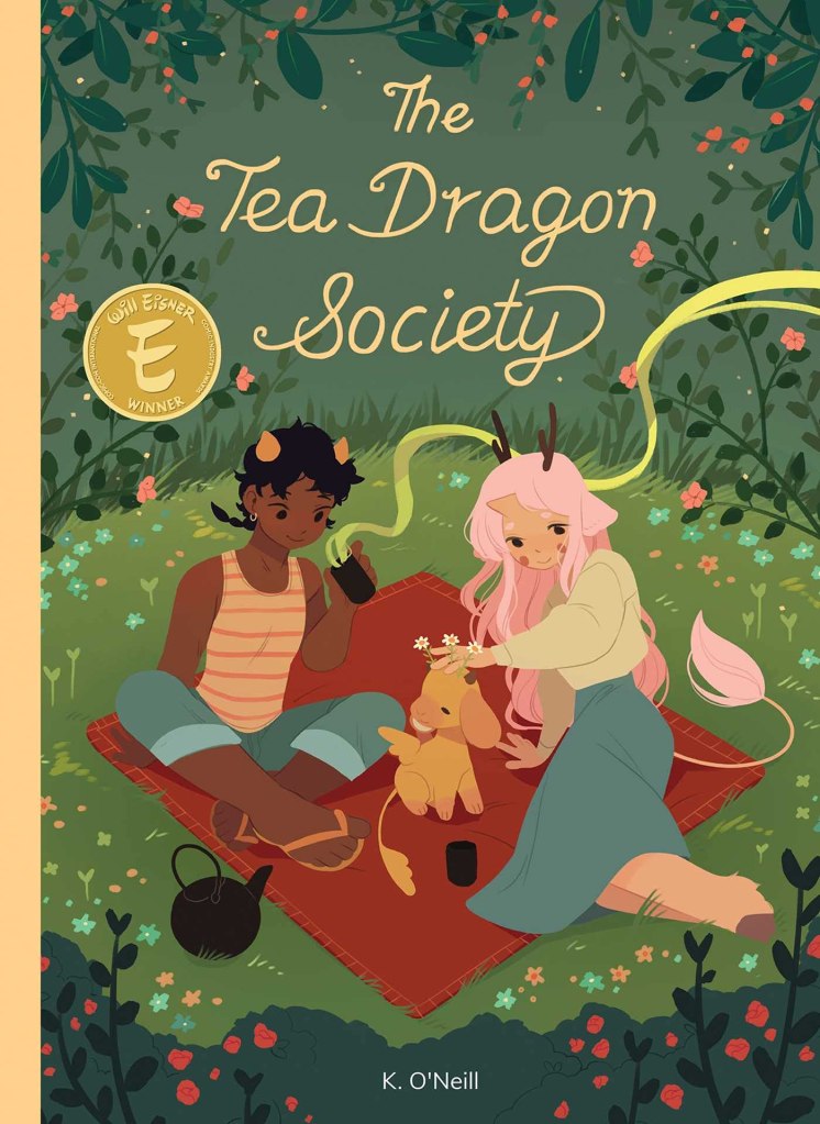 Book Cover of The Tea Dragon Society: two girls sitting on blanket with small dog-like dragon. They are surrounded by flowers and have a teapot with teacups. One of the girls has pink hair, deer antlers, hooves, and a tail. The other girl has brown pig-tails and orange pointed horns. 